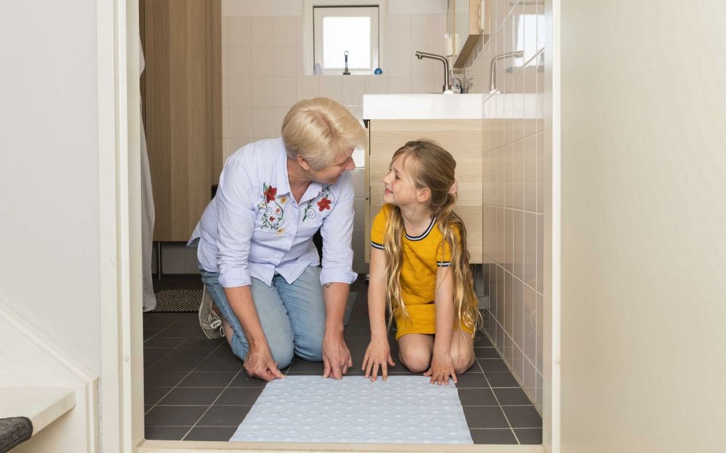 Foto van oma en kleindochter die antisliplaag aan de onderkant van kleed bevestigen.